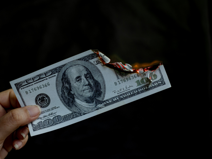 Burning $100 bill held against a dark background.